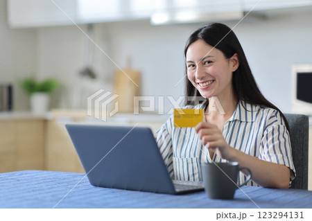 Happy asian woman holding credit card using laptop looking at you 123294131