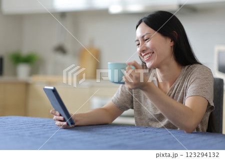 Happy asian woman reading ebook drinking in the kitchen 123294132