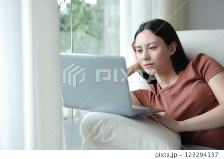 Serious asian woman using laptop relaxed on a couch Serious asian woman using laptop relaxed on a couch 123294137