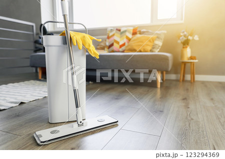 Cleaning supplies: mop, gloves, bucket with wringer sitting on wooden laminate floor in modern living room, wet equipment tools, housekeeping concept. Emphasizing home sanitation, cleanliness, hygiene 123294369