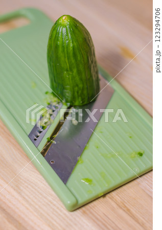 Fresh green cucumber on a light green mandoline slicer, ready for slicing . High quality photo 123294706