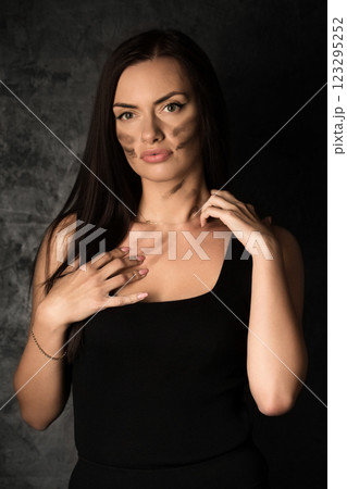 Beautiful woman in a black top applying camouflage military makeup to her body 123295252