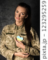 Beautiful military woman in military uniform with camouflage makeup on her face holds a heart-shaped Ukrainian flag in her hands 123295259