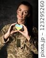 Military woman in military uniform with camouflage makeup on her face holds a heart-shaped Ukrainian flag in her hands 123295260