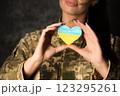 Military woman in military uniform with camouflage makeup on her face holds a heart-shaped Ukrainian flag in her hands. Close-up 123295261