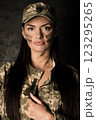 Portrait of a young woman in a military uniform and a cap with the coat of arms of Ukraine. The woman has camouflage on her face 123295265