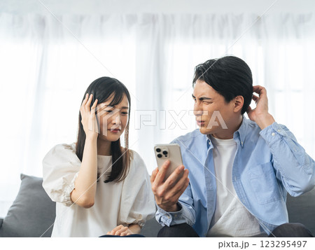 リビングルームでスマホを見ながら悩むカップル 123295497