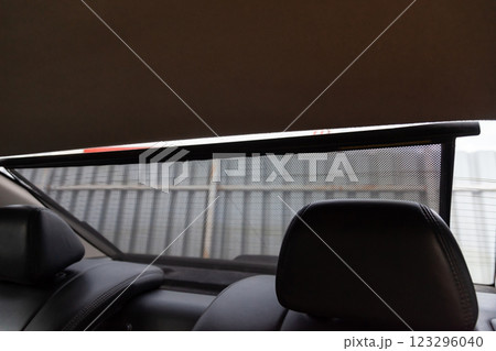 Automatic electric Sunblind on the glass of the rear window of the car black color close-up protects from the sun rays textured double mesh of a special material. Auto service industry. 123296040