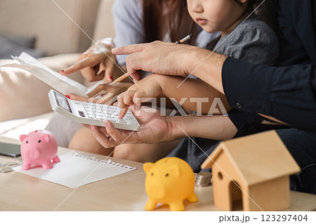 Family using calculator and piggy banks to teach children about saving money. 123297404