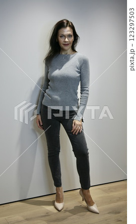 Positive woman 51 years old with evening make-up in a grey sweater and jeans in pink high-heeled shoes posing and looking at the camera Positive woman 51 years old with evening make-up in a grey sweater and jeans in pink high-heeled shoes posing and looking at the camera 123297503