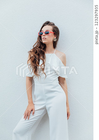 Beautiful brunette woman in white suit posing by the wall with plants 123297935