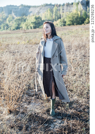 Beautiful brunette woman in gray coat walking in rural field Beautiful brunette woman in gray coat walking in rural field 123298236
