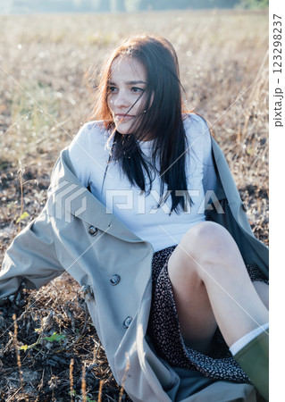 Beautiful fashionable brunette woman in gray coat sitting on the ground Beautiful fashionable brunette woman in gray coat sitting on the ground 123298237