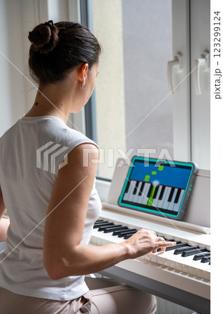 Young woman learning to play the keyboard at home using an interactive app. Using mobile apps for self-study concept Young woman learning to play the keyboard at home using an interactive app. Using mobile apps for self-study concept 123299124