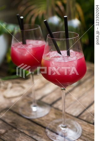 Red cocktail with ice in glass with stem on wooden surface 123302004