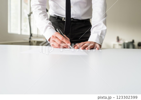 Businessman standing behind his office desk signing a document 123302399