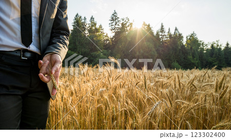 Businessman standing on the left side of an image touching golden ear of wheat 123302400