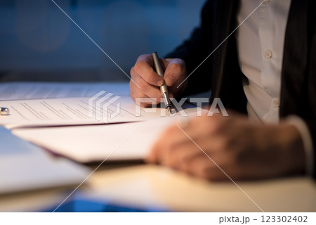 Businessman working late signing a document or contract Businessman working late signing a document or contract 123302402