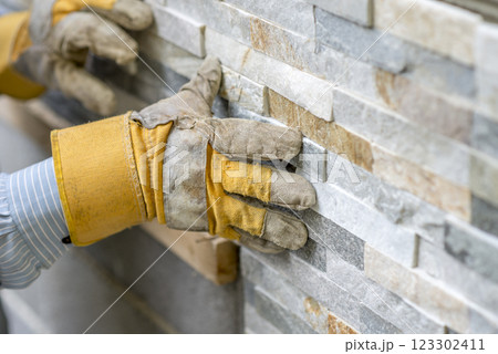 Closeup of manual worker in protection gloves pushing the tile into the cement on the wall Closeup of manual worker in protection gloves pushing the tile into the cement on the wall 123302411