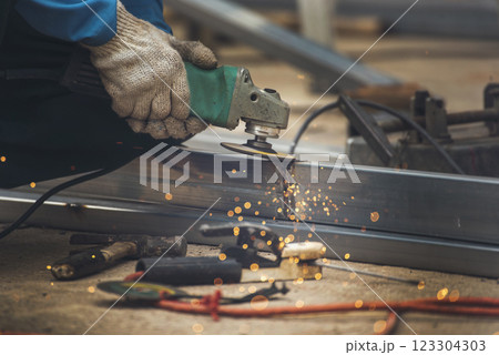 Construction Worker hands using Welding machinery iron metal sparking. Men hands wear protective glove Hot flame metal work cutting fire iron workshop. Locksmith use Welding machine cut metal process 123304303