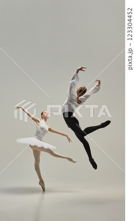Poised ballerina on pointe with male partner leaping beside, showcasing contrast between lightness and strength against white studio background. 123304452