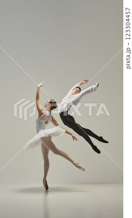 Young ballet dancers in mid-air, reaching arms upward as bodies align in striking balance against white studio background. Concept of classic art and beauty. Young ballet dancers in mid-air, reaching arms upward as bodies align in striking balance against white studio background. Concept of classic art and beauty. 123304457