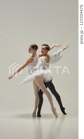 Ballet partners moving in perfect harmony, arms extended with fluid motion, bodies intertwining in elegant balance against white studio background. 123304478