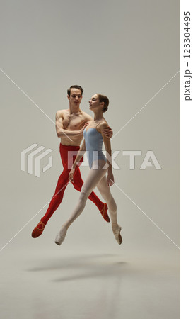Dynamic photo of young ballet duo, athletic man and woman, leaping in motion gracefully in synchronized motion against white studio background. 123304495