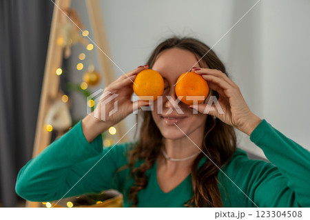 Woman Oranges Christmas Festive Playful Portrait: Indoor Holiday Cheer, Woman playfully covering eyes with oranges near Christmas tree. Woman Oranges Christmas Festive Playful Portrait: Indoor Holiday Cheer, Woman playfully covering eyes with oranges near Christmas tree. 123304508