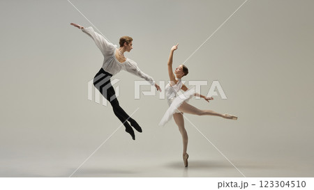 Gravity-defying motion. Ballet duet in poetic airborne movement, arms extended, legs reaching outward against white studio background. 123304510
