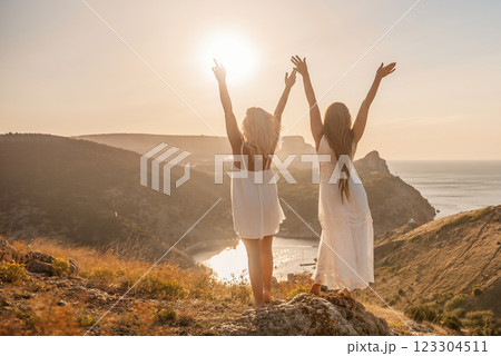 Two women are standing on a hill overlooking the ocean. They are holding hands and looking out at the water. The scene is peaceful and serene, with the sun shining brightly in the background. Two women are standing on a hill overlooking the ocean. They are holding hands and looking out at the water. The scene is peaceful and serene, with the sun shining brightly in the background. 123304511