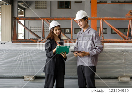 Two worker in hardhat talk in a warehouse. They discuss plans while standing near large, wrapped material. 123304930