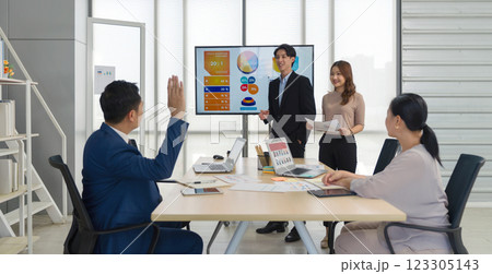 Senior asian businessman in suit raise his hand to ask a question to presenter standing in front of a large digital monitor. Business executive team meeting in modern office. Senior asian businessman in suit raise his hand to ask a question to presenter standing in front of a large digital monitor. Business executive team meeting in modern office. 123305143