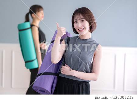 ヨガマットを持ちながらグッドポーズする笑顔の若い女性 123305218
