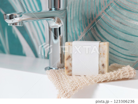 Beige soap with blank label on soap saver bag on basin in green tropical bathroom close up, mockup 123306236
