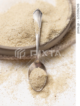 Raw uncooked fonio seeds on a plate with a metal spoon on white table. African ancient pseudocereal 123306246