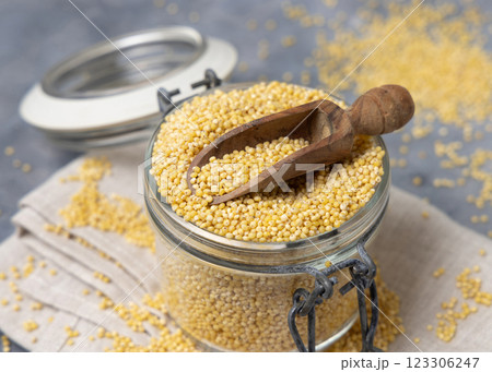 Glass jar of raw uncooked yellow millet grain with a wooden scoop closeup. Ancient food 123306247