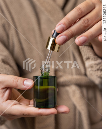 Closeup of woman in brown bathrobe opening green dropper bottle, cosmetic mockup 123306248