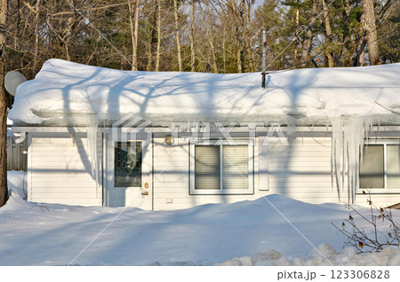 Large icicles and ice dams form at the edge of the snow-covered roof above frozen eavestrough gutter 123306828