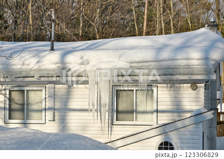 Large icicles and ice dams form at the edge of the snow-covered roof above frozen eavestrough gutter Large icicles and ice dams form at the edge of the snow-covered roof above frozen eavestrough gutter 123306829