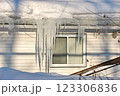 Large icicles and ice dams form at the edge of the snow-covered roof above frozen eavestrough gutter 123306836
