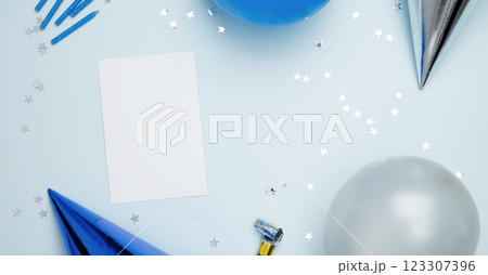Concept of festive birthday celebrations. Blank card surrounded by colorful balloons, party hats, candles, confetti 123307396