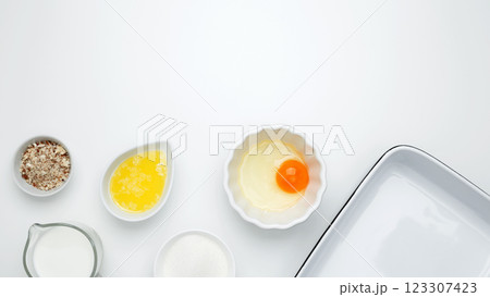 Flat lay composition for cooking preparation. Empty white baking dish with ingredients for baking, including egg, milk, butter, sugar, nuts 123307423
