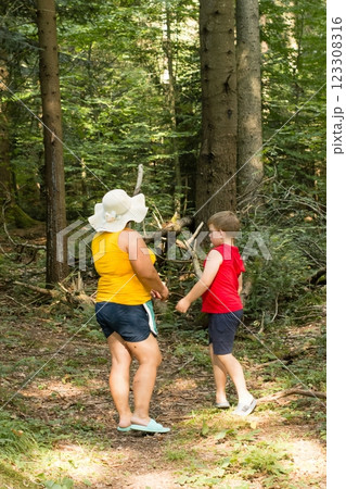 A woman and a child stroll through a sun-dappled forest, enjoying a peaceful woodland walk. A woman and a child stroll through a sun-dappled forest, enjoying a peaceful woodland walk. 123308316