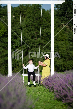 A woman helps a child on a swing in a lavender field. A sunny day, joyful moment. 123308323