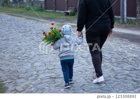 A toddler holds flowers while walking hand-in-hand with an adult on a cobblestone street, capturing a tender moment of family connection. 123308891