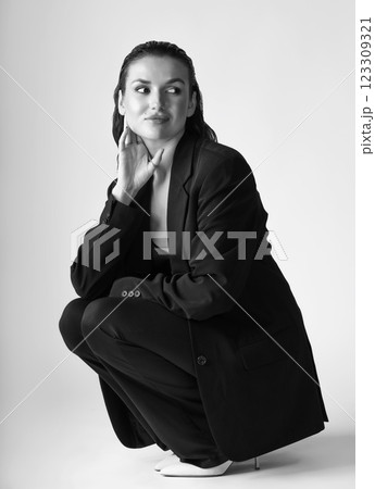 Studio portrait of beautiful woman with black suit and wet hair squatting on floor Studio portrait of beautiful woman with black suit and wet hair squatting on floor 123309321