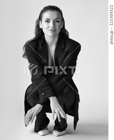 Studio portrait of beautiful woman with black suit and wet hair squatting on floor Studio portrait of beautiful woman with black suit and wet hair squatting on floor 123309322