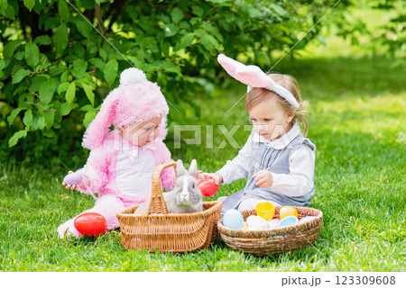 Children play with real rabbit. Laughing child at Easter egg hunt with pet bunny. Little toddler girl playing with animal in garden. Cute funny girl with Easter eggs and bunny ears at garden. 123309608