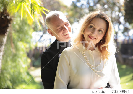 Priest smiling and embracing elegant woman in garden setting Priest smiling and embracing elegant woman in garden setting 123309966